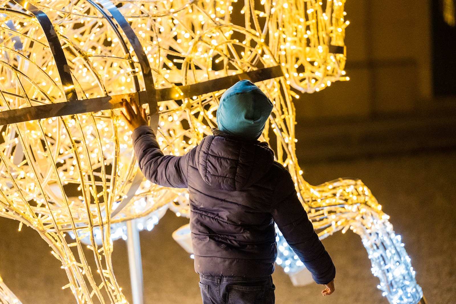 Ein Kind greift nach einer leuchtenden Kutschenskulptur aus goldenem Lichtdraht