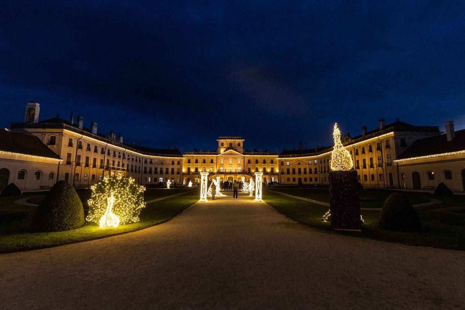 Das barocke Schloss Esterházy in Fertőd zur blauen Stunde, beleuchtete Fassade und ein leuchtender Baum im symmetrischen Garten