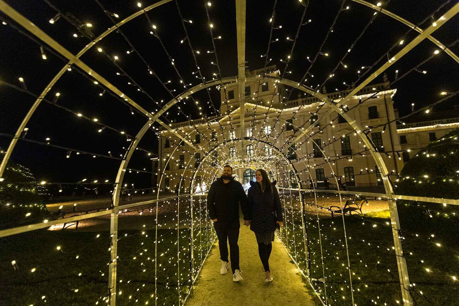 Ein Tunnel aus Lichtbögen über einem Weg im Schlosspark, zwei Besucher gehen hindurch